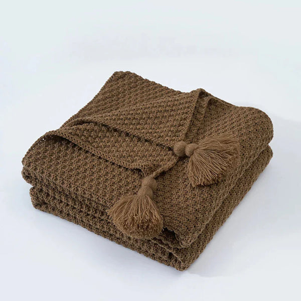 Gevouwen bruine gebreide deken met kwastjes, perfect voor interieurdecoratie en comfort. Ideaal voor woonkamer of slaapkamer styling.