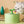 Witte kat drinkt uit groene kattenfontein met plantenmotief, naast houten boomdecoratie. Ideaal voor huisdieren, modern design, waterfontein.