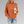 Oranje gebreide trui met col, gedragen door vrouw met blond haar, gecombineerd met gescheurde jeans en een kartonnen koffiebeker. Trendy herfstmode.
