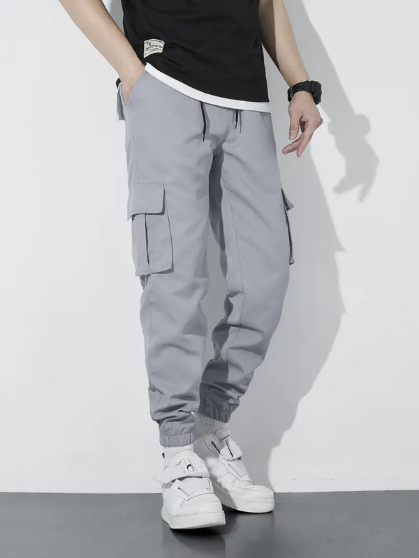 Grijze cargo joggingbroek voor heren met elastische tailleband en zakken, gecombineerd met witte sneakers. Comfortabele streetwear-stijl.