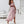 Vrouw in roze off-shoulder jurk met ruches, staand in moderne witte woonkamer. Elegante zomeroutfit, hoge hakken, stijlvolle mode.