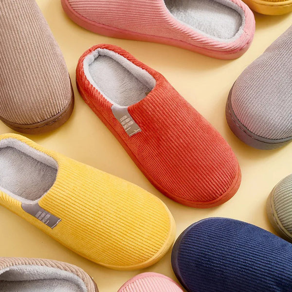 Verschillende kleurrijke corduroy pantoffels op een gele achtergrond, inclusief rode, gele, blauwe en roze slippers. Comfortabele huispantoffels.