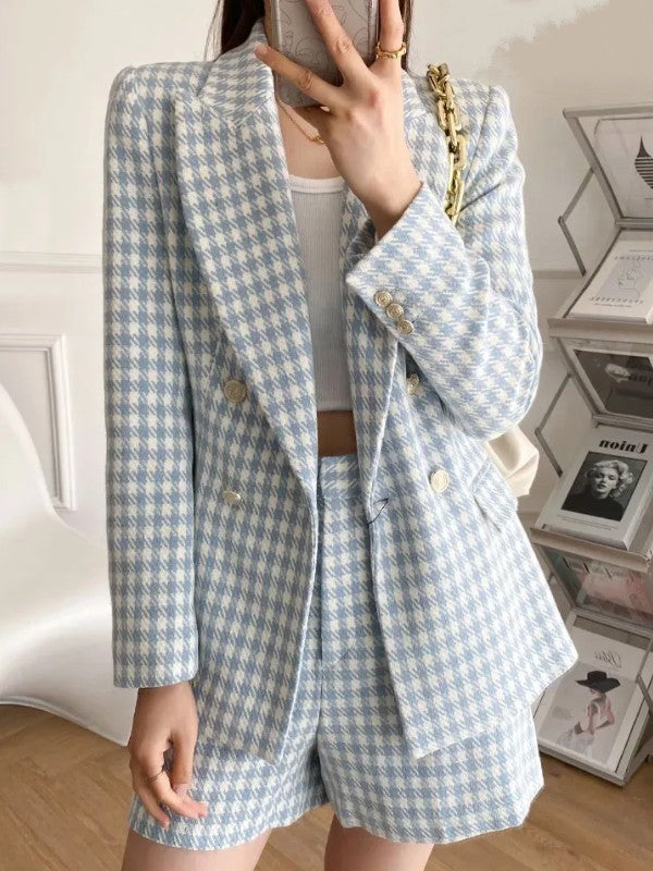 Vrouw in blauw-wit geruit pak met gouden knopen, witte top en beige tas. Trendy damesmode, stijlvolle blazer en korte broek.