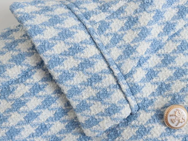 Blauw-wit pied-de-poule jasje met gouden knoop, close-up. Luxe damesmode, elegante textuur, stijlvolle jas, hoogwaardige stof.