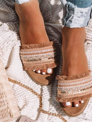 Beige sandalen met franjes en etnisch patroon, gedragen door vrouw op gebreide deken. Zomerschoenen, boho-stijl, casual mode.