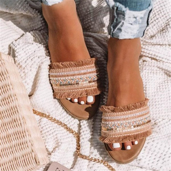 Beige sandalen met franjes en etnisch patroon, gedragen door vrouw op gebreide deken. Zomerschoenen, boho-stijl, casual mode.