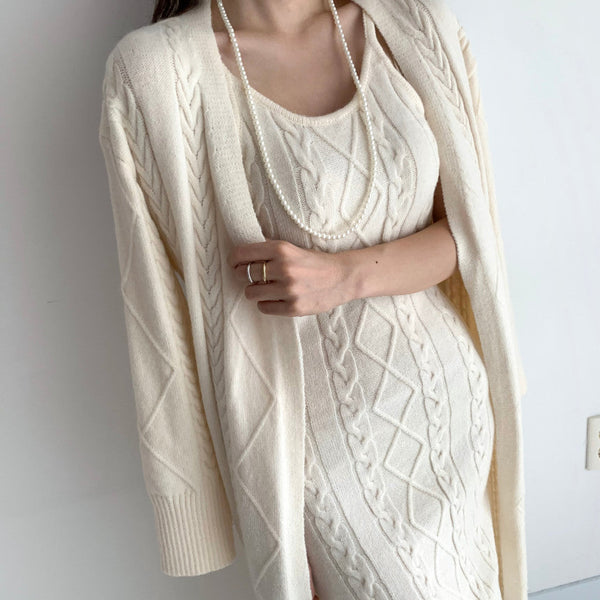 Vrouw in beige gebreide jurk met kabelpatroon, lange mouwen en parelketting. Elegante herfstmode, stijlvolle dameskleding.