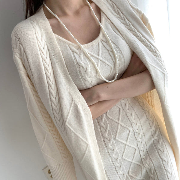 Vrouw in elegante beige kabeltrui jurk met lange mouwen en parelketting, stijlvolle herfstmode, comfortabele en chique dameskleding.