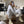 Vrouw in witte loungewear en beige laarzen, zittend op een poef in een moderne woonkamer. Trendy mode, comfortabele kleding, minimalistisch interieur.