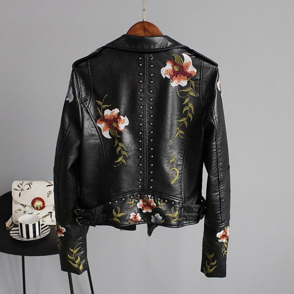 Zwarte leren jas met bloemenborduursels en studs, hangend aan een hanger. Trendy damesmode, bikerstijl, perfect voor casual en edgy looks.