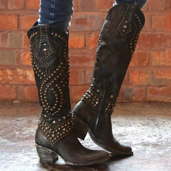 Zwarte leren laarzen met studs, hoge hak en ritssluiting, tegen een bakstenen muur. Trendy dameslaarzen, westernstijl, modieuze schoenen.