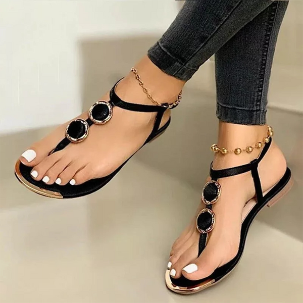 Zwarte sandalen met gouden details en zwarte stenen, gedragen door een vrouw met witte nagellak. Stijlvolle zomerschoenen voor dames.