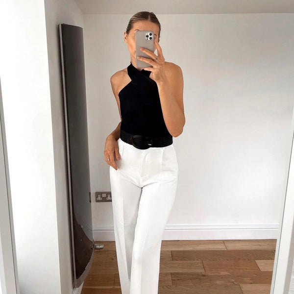 Vrouw in stijlvolle zwarte haltertop en witte broek, poseert voor een spiegel. Moderne mode, minimalistisch design, trendy outfit.