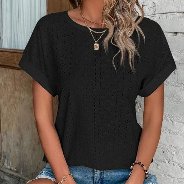 Vrouw in zwarte geperforeerde blouse, korte mouwen, gouden ketting, casual look, zomermode, trendy dameskleding, denim shorts.