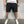 Man in zwarte korte broek en witte sneakers tegen grijze achtergrond. Casual zomeroutfit, comfortabele streetwear, mode voor heren.