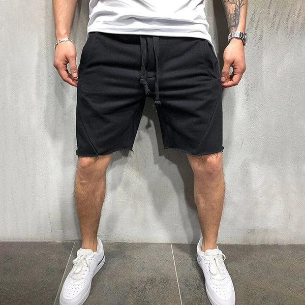 Man in zwarte korte broek en witte sneakers tegen grijze achtergrond. Casual zomeroutfit, comfortabele streetwear, mode voor heren.