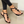 Zwarte sandalen met gouden details en zwarte stenen, gedragen door een persoon met witte nagellak. Trendy zomerschoenen voor dames.