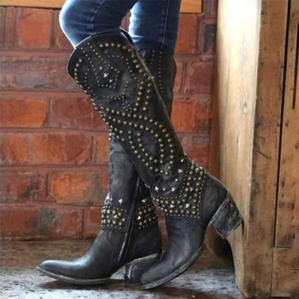 Zwarte leren laarzen met studs, gedragen door persoon tegen bakstenen muur. Trendy dameslaarzen, westernstijl, perfect voor casual en stoere outfits.