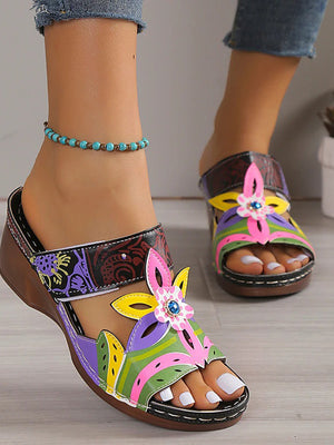 Vrouw draagt kleurrijke sandalen met bloemenpatroon en sleehak, perfect voor zomermode. Comfortabele open teen design, ideaal voor casual outfits.