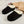 Zwarte pantoffels met witte voering op een beige tapijt, naast een gevlochten mand en bloemen. Comfortabele winterse huisschoenen.