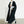 Zwarte gebreide lange cardigan, oversized pasvorm, gedragen door vrouw met witte coltrui en broek, minimalistische mode, herfst-winter stijl.