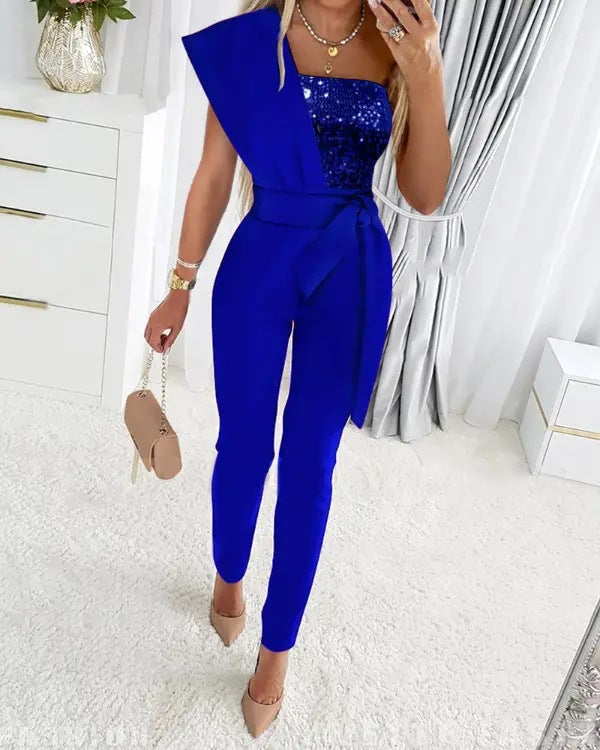 Blauwe jumpsuit met asymmetrisch ontwerp en pailletten top, gedragen door vrouw met beige handtas en hakken, elegante mode voor dames.