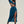 Vrouw in elegante blauwe jurk met hoge split en lange mouwen poseert op marmeren platform. Trendy mode, zomerjurk, stijlvolle outfit.