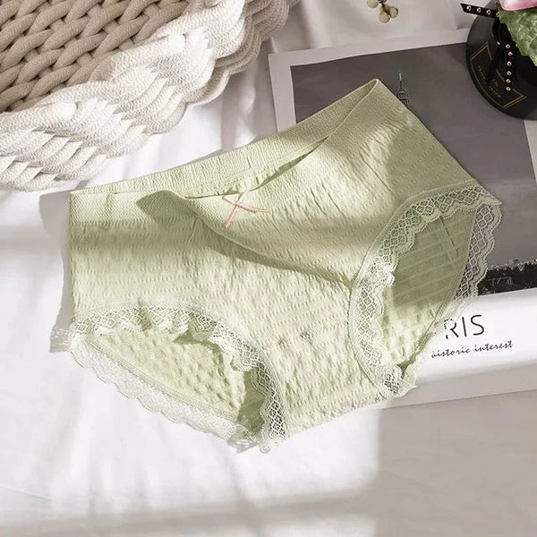 Lichtgroene damesonderbroek met kantdetails op een witte achtergrond, naast een tijdschrift en decoratieve mand. Comfortabel en stijlvol ondergoed.