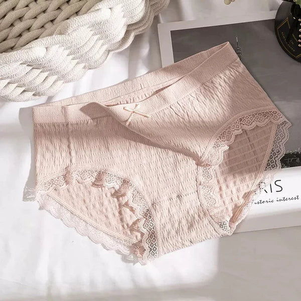Roze damesondergoed met kanten details op een witte achtergrond, naast een gebreide deken. Comfortabel en stijlvol lingerieontwerp.