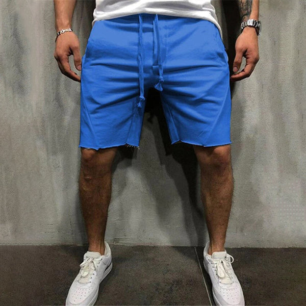 Man in blauwe korte broek en witte sneakers tegen grijze achtergrond. Casual zomeroutfit, mode voor heren, comfortabele sportieve stijl.