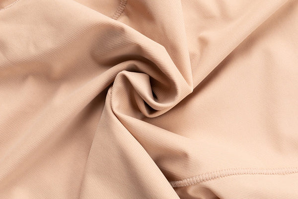 Beige stretchstof close-up, gedrapeerd en geplooid, ideaal voor kleding en modeontwerp. Elastische textieltextuur, naad zichtbaar.
