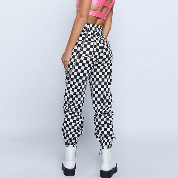 Vrouw in zwart-wit geruite broek, roze crop top en witte laarzen. Modieuze streetwear outfit, trendy dameskleding, casual stijl.