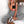 Vrouw in zwart crop top en geruite broek, zittend op keukenblad. Modieuze outfit, casual stijl, trendy sneakers. Perfect voor streetwear inspiratie.