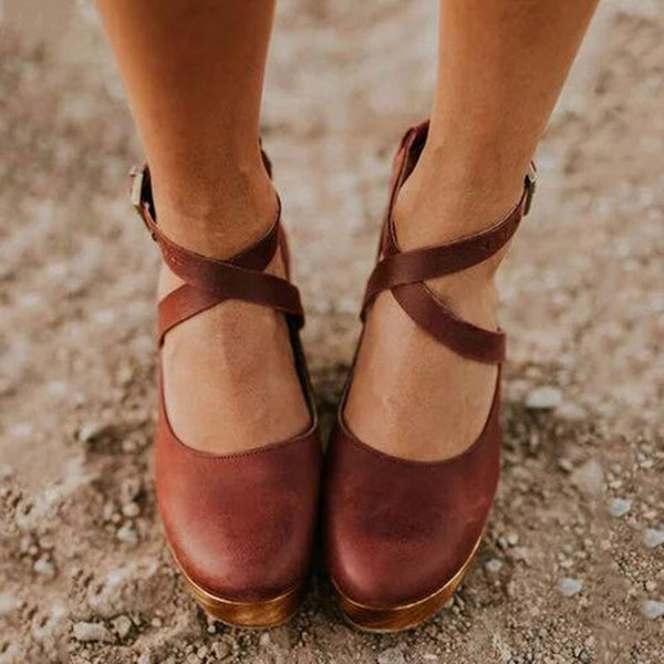 Bruine leren damesschoenen met kruisbandjes, gedragen op een zanderige ondergrond. Comfortabele, stijlvolle schoenen voor dagelijks gebruik.
