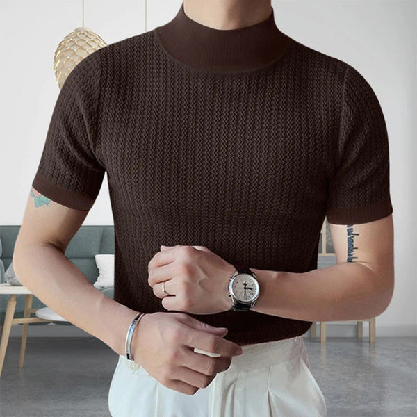 Man in bruine gebreide trui met korte mouwen, draagt een zilveren horloge en armband, moderne woonkamer op de achtergrond. Mode, herenkleding, stijlvol.