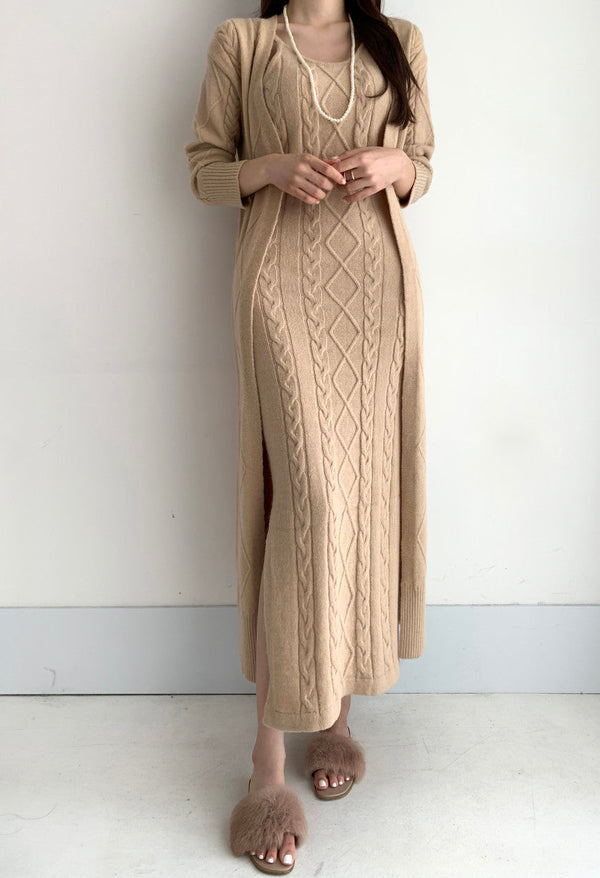Vrouw in beige gebreide jurk met kabelpatroon en lange mouwen, gecombineerd met bijpassende vest en pluizige slippers. Elegante herfstmode.