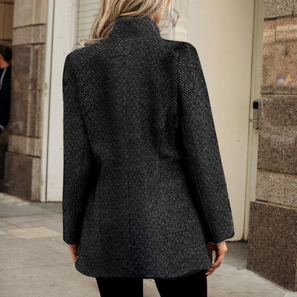 Vrouw in zwarte wollen jas met visgraatpatroon, staand op straat. Stijlvolle wintermode, dameskleding, buitenkleding, trendy jas.