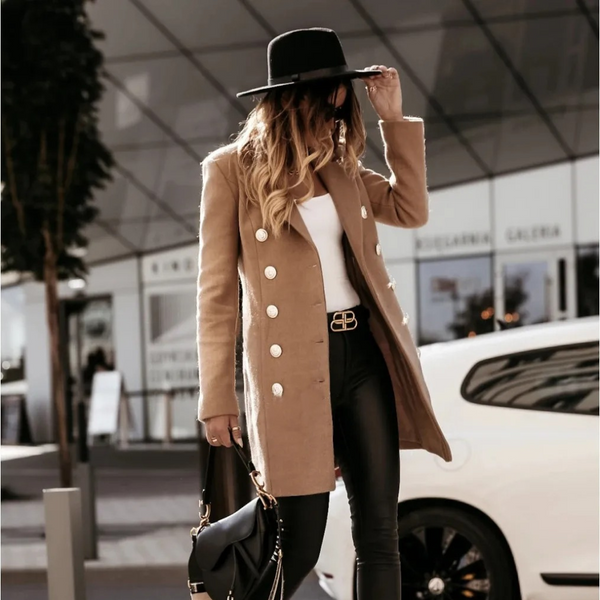 Vrouw in stijlvolle camel jas met dubbele rij knopen, zwarte hoed en leren broek, poseert voor luxe auto. Mode, herfstkleding, stedelijke stijl.