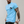 Man in lichtblauw T-shirt met palmboomprint, getatoeëerde armen, zilveren ketting en horloge. Modieuze herenkleding, casual stijl.