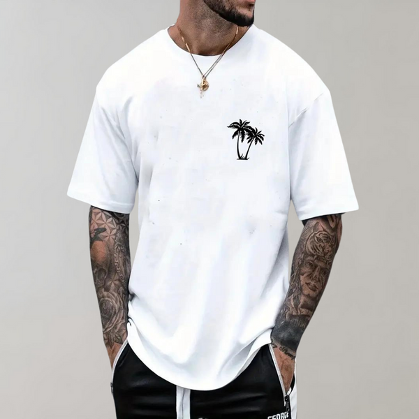 Witte T-shirt met palmboomprint, gedragen door getatoeëerde man. Casual herenmode, zomerse stijl, korte mouwen, comfortabele pasvorm.