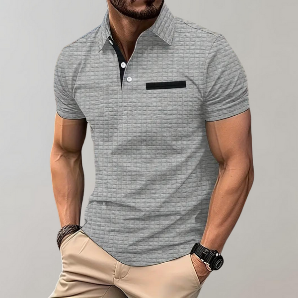 Grijze herenpolo met korte mouwen, zwarte borstzakdetail, gedragen door een man. Stijlvolle casual outfit, ideaal voor mode en comfort.