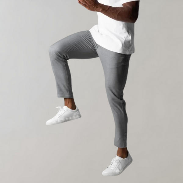 Man in grijze broek en witte sneakers springt in de lucht tegen een neutrale achtergrond. Stijlvolle casual mode, comfortabele kleding.