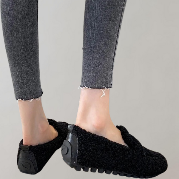 Zwarte damespantoffels met rubberen zool, gedragen door model met grijze jeans. Comfortabele, warme sloffen voor thuisgebruik.