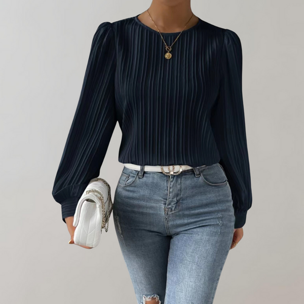 Vrouw in donkerblauwe geplooide blouse met lange mouwen, draagt een witte tas en spijkerbroek. Modieuze dameskleding, casual chic stijl.