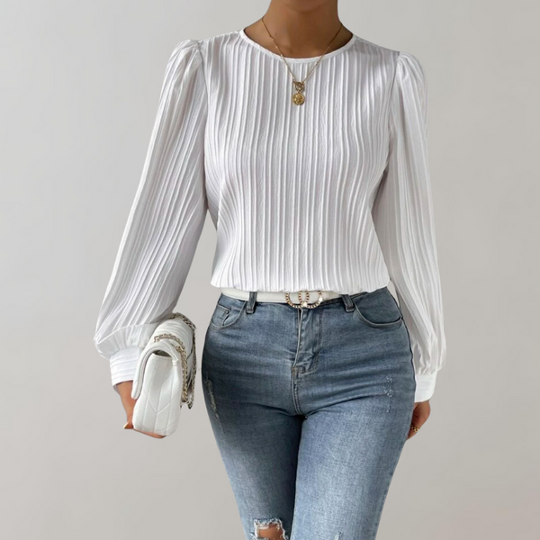 Vrouw in witte, geplooide blouse met lange mouwen en blauwe jeans, draagt een witte handtas en gouden ketting. Elegante damesmode, casual chic.