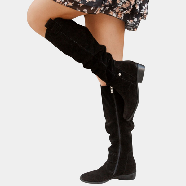 Zwarte suède laarzen met rits en gesp, gedragen door model in bloemenjurk. Stijlvolle damesmode, herfst/winter schoenen.