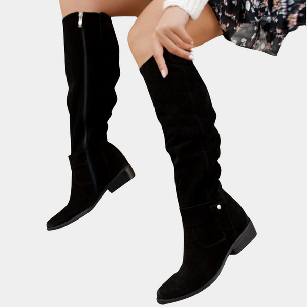 Zwarte suède knielaarzen met ritssluiting, gedragen door model in bloemenjurk. Stijlvolle dameslaarzen voor herfstmode.