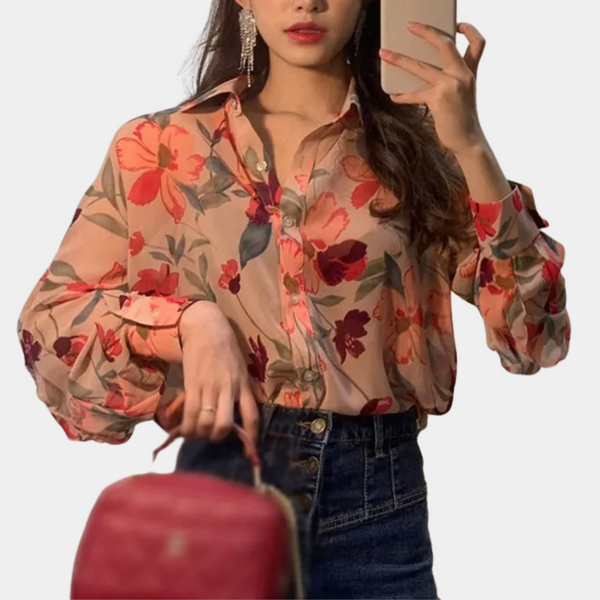 Vrouw in bloemenblouse met lange mouwen, houdt rode tas vast, maakt selfie. Modieuze dameskleding, casual stijl, trendy outfit.