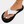 Beige leren slipper met zwarte zool en witte band, gedragen aan een voet met witte nagellak en enkelbandje. Stijlvolle zomerschoen voor dames.