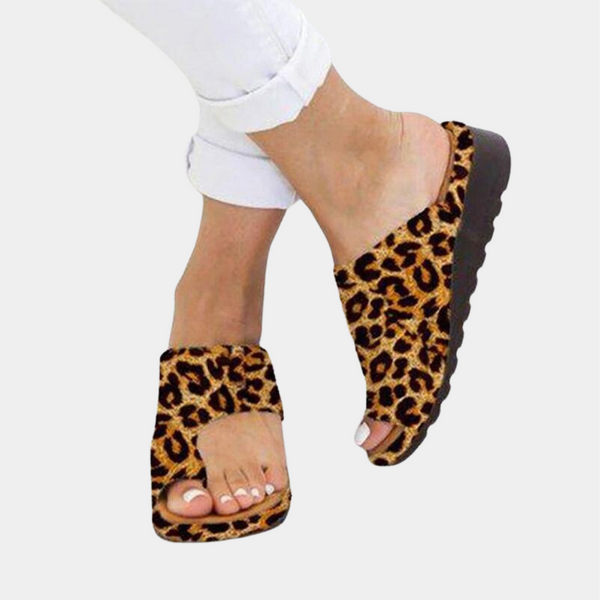Vrouwelijke voeten in witte jeans dragen luipaardprint slippers met dikke zool, modieuze zomerschoenen, comfortabele sandalen voor dames.